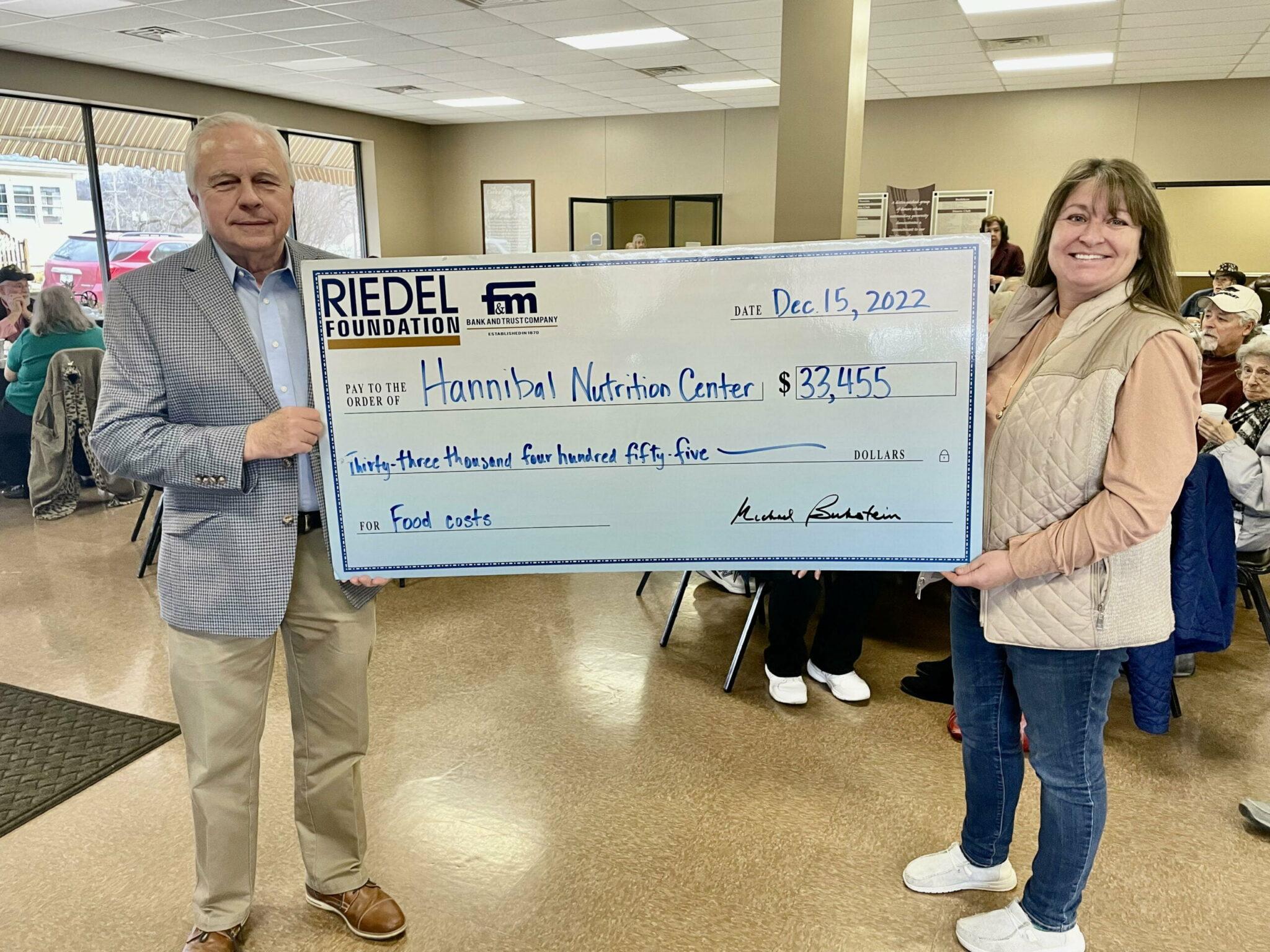 Riedel Foundation Trustee Bill Craigmiles presents a check to Hannibal Nutrition Center Executive Director Margee Tucker at its recent Christmas dinner.