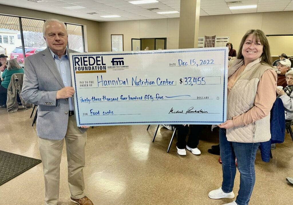 Riedel Foundation Trustee Bill Craigmiles presents a check to Hannibal Nutrition Center Executive Director Margee Tucker at its recent Christmas dinner.